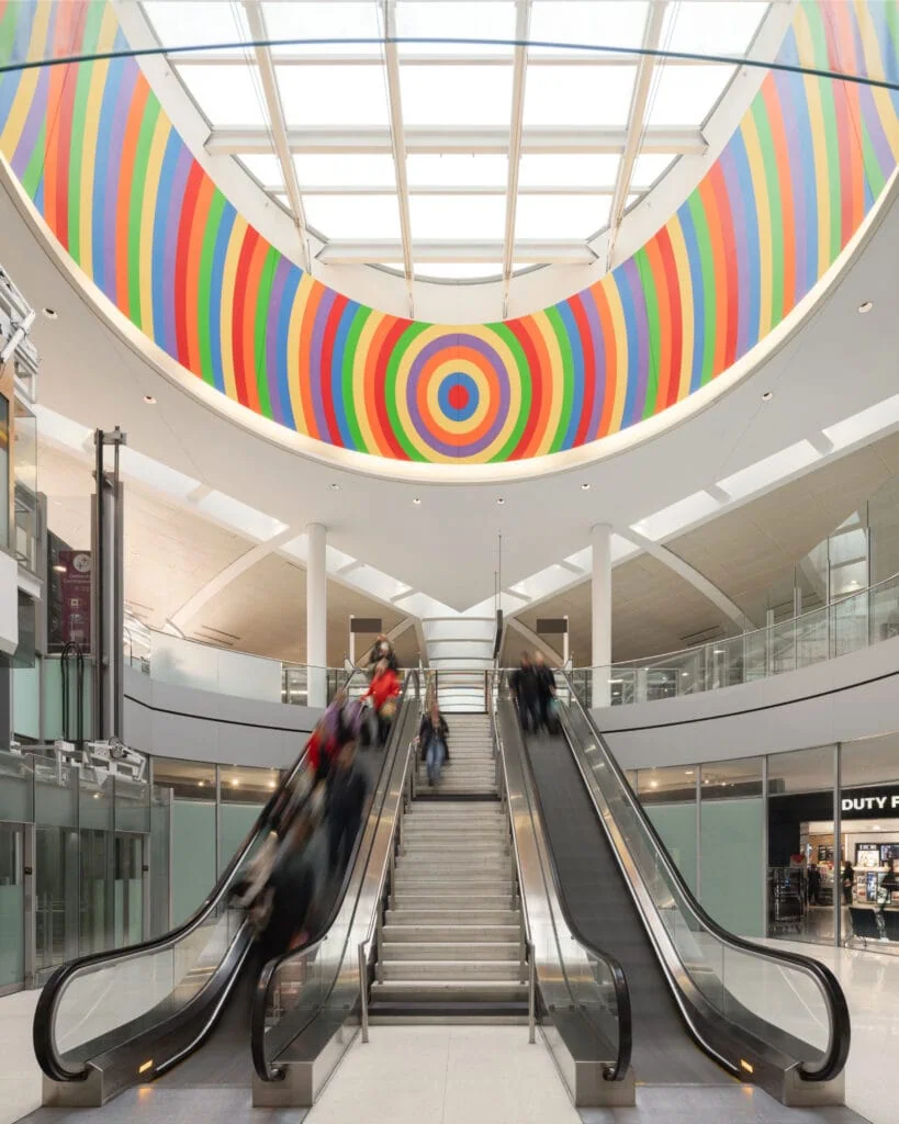 Escalators in Toronto Pearson airport beneath a colorful circular Sol LeWitt mural and skylight.